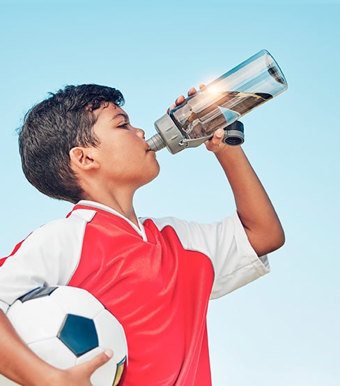 boy holding soccer ball and drinking water